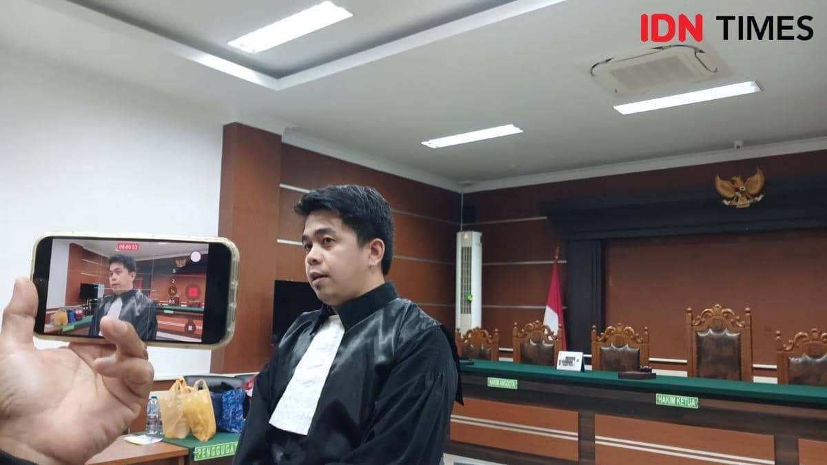 Seorang pria mengenakan toga hitam berdiri di ruang sidang Pengadilan Negeri Manado, sementara seseorang merekamnya menggunakan ponsel.