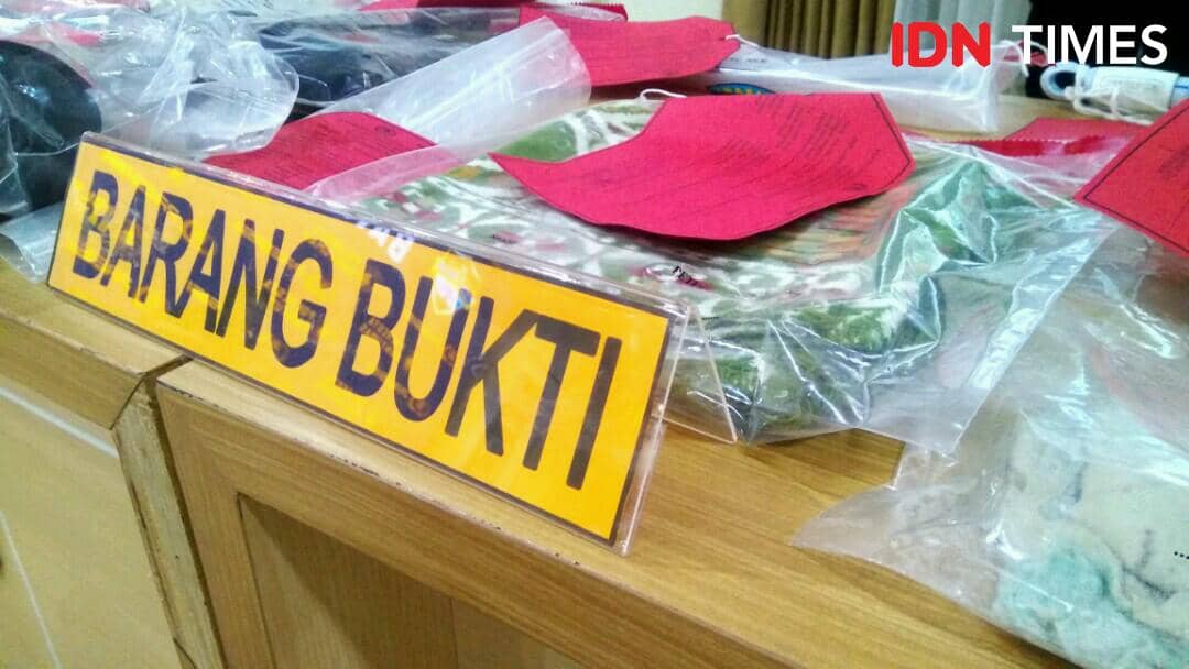 Barang bukti kasus pembunuhan di Patikraja berupa sajadah dan palu yang dibungkus plastik dengan label dan tanda bukti di atas meja kayu.
