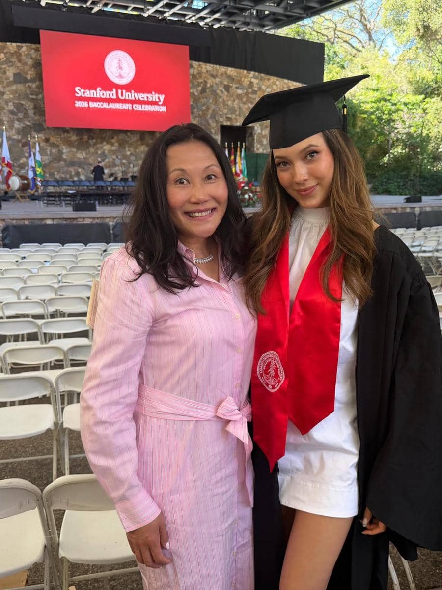 Seorang lulusan Stanford University mengenakan toga hitam dan selempang merah berfoto bersama seorang wanita di acara wisuda.