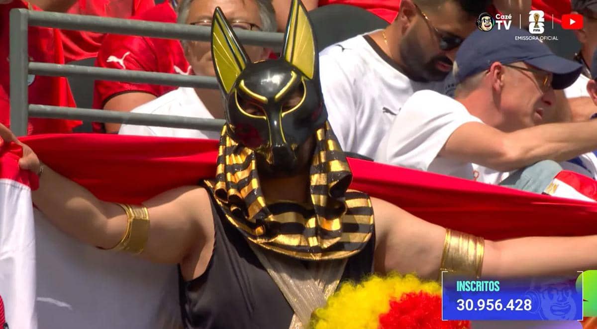 Penonton Piala Dunia 2026 mengenakan kostum unik bergaya Mesir dengan topeng hitam emas dan aksesori emas di tengah tribun stadion.