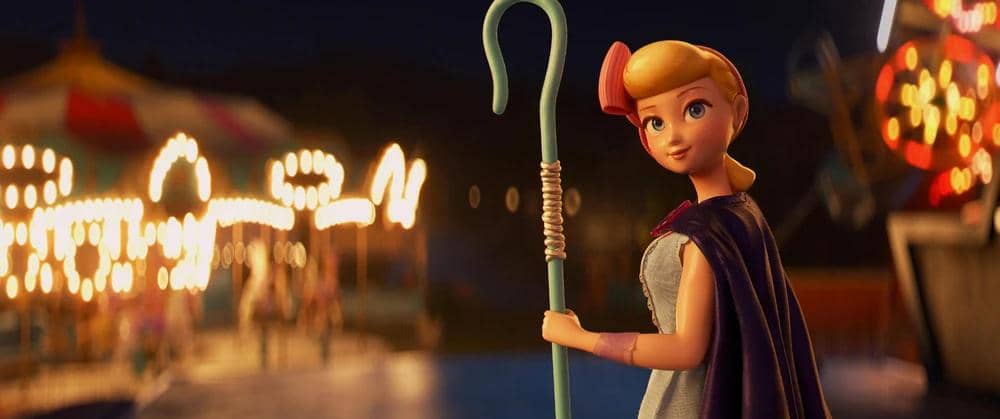 Karakter animasi Bo Peep memegang tongkat gembala di malam hari dengan latar lampu taman bermain yang berwarna-warni.