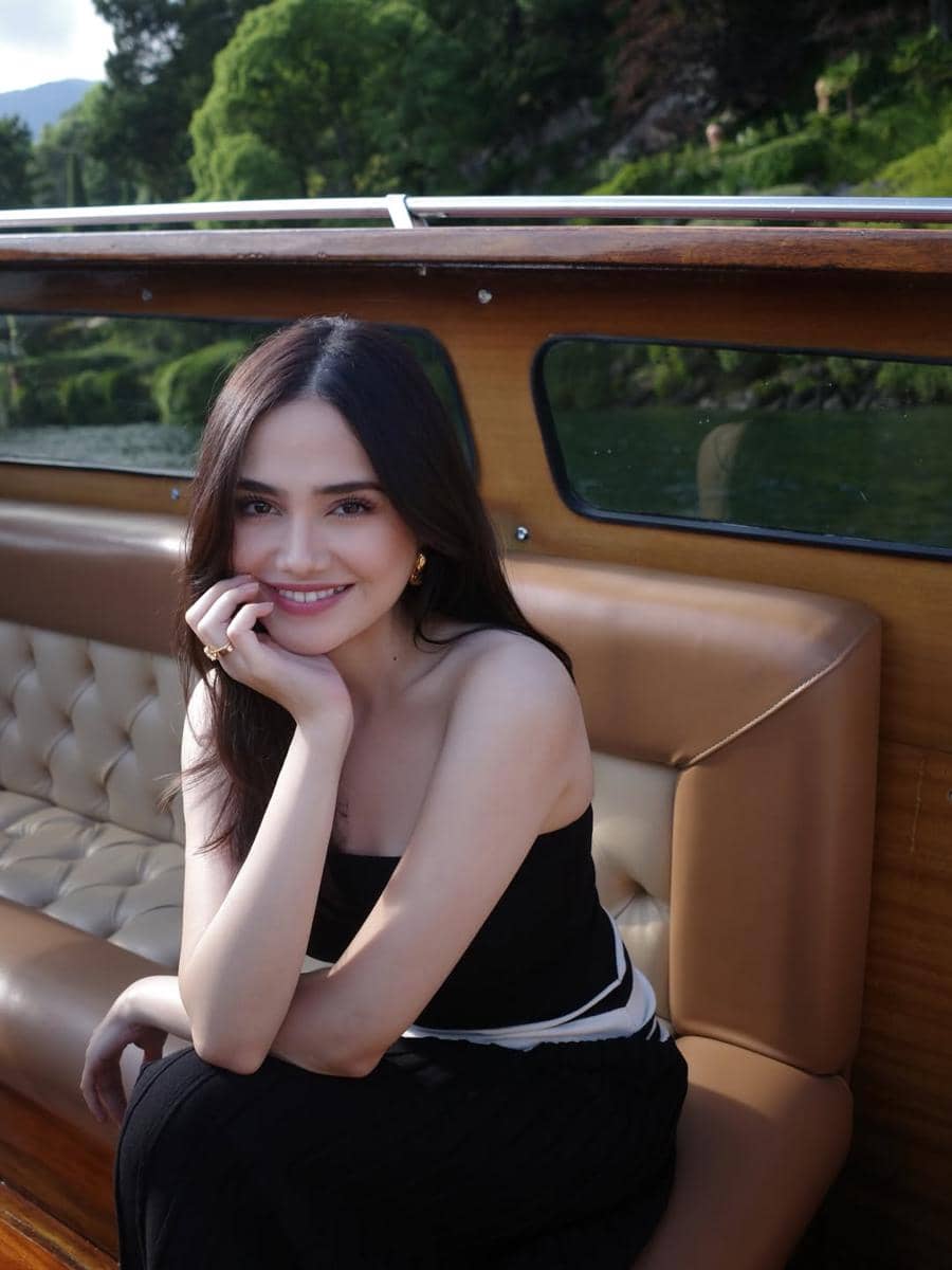 Syifa Hadju berambut panjang mengenakan pakaian hitam duduk di perahu kayu dengan latar pepohonan hijau di Lake Como.