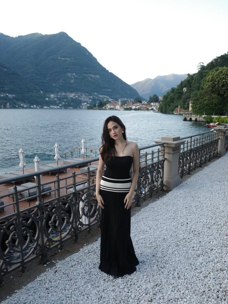 Syifa Hadju mengenakan gaun hitam tanpa lengan berdiri di tepi danau dengan latar pegunungan hijau di Lake Como, Italia.