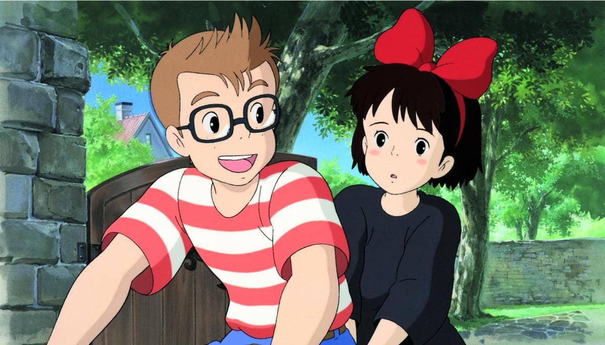 Kiki dan Tombo Kopoli dari film Kiki's Delivery Service sedang berbincang di luar ruangan dengan latar pepohonan hijau dan dinding batu.