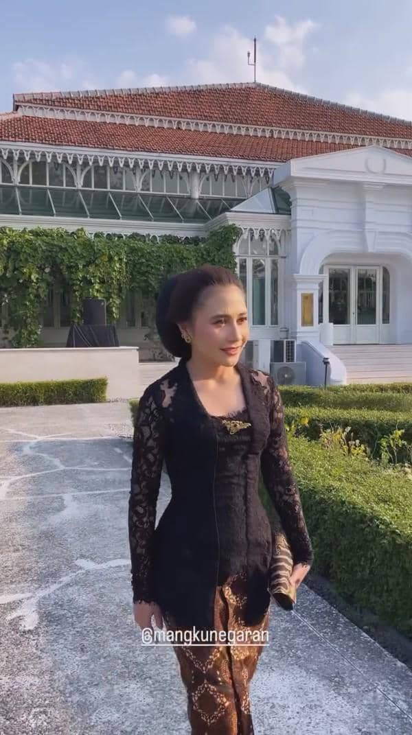 Seorang perempuan mengenakan kebaya hitam dan kain batik berjalan di area Mangkunegaran saat perayaan Kirab Pusaka Dalem Malam 1 Suro.