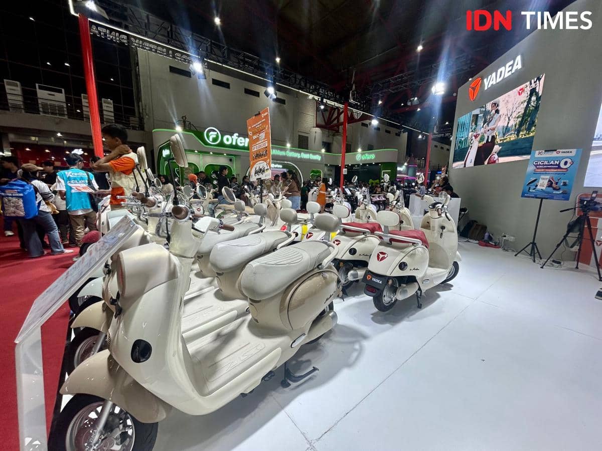Deretan skuter listrik Yadea berwarna krem dipamerkan di booth pameran dengan layar besar dan pengunjung yang berinteraksi di sekitarnya.