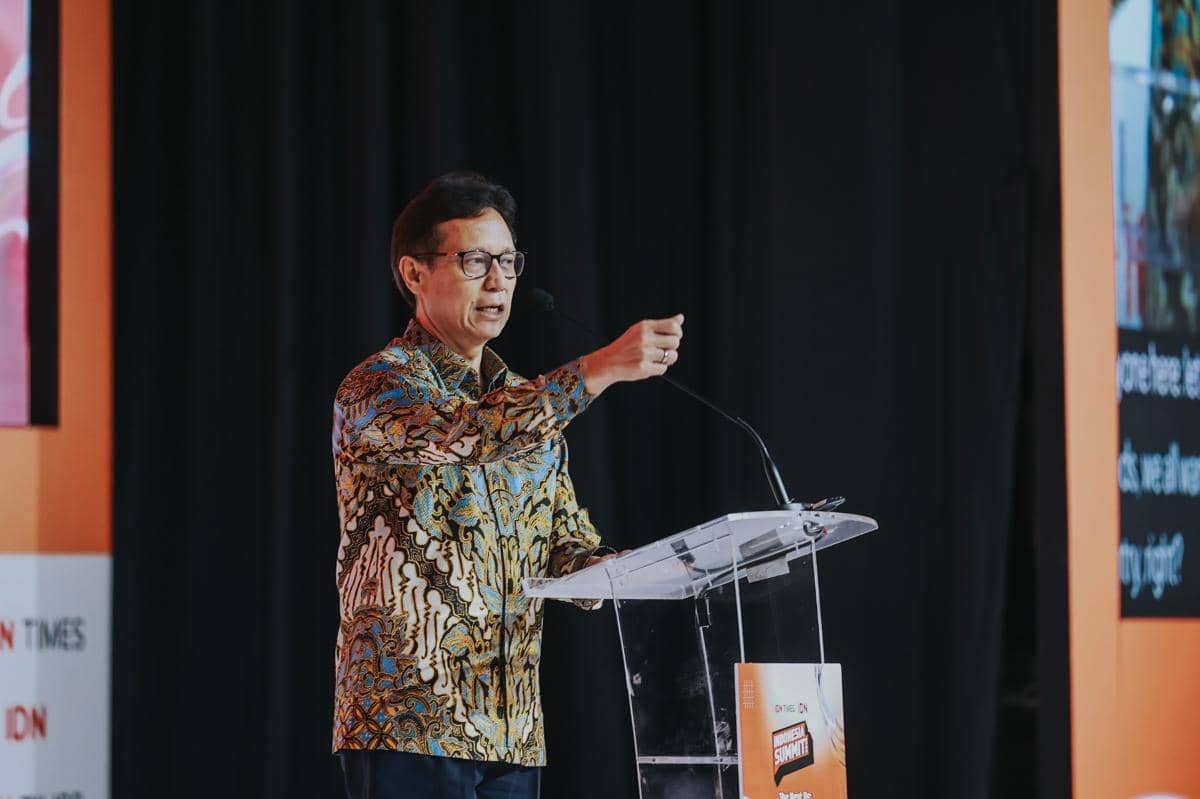 Seorang pria mengenakan batik berbicara di podium dengan latar belakang hitam dan oranye pada acara Indonesia Summit 2026.