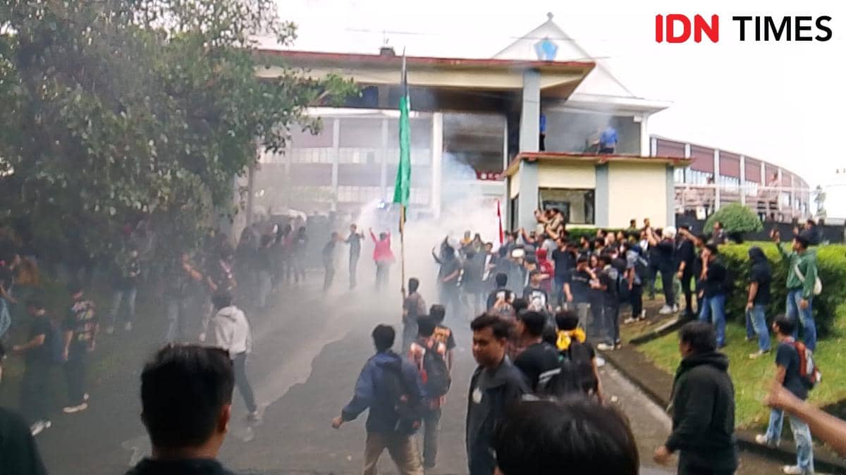 Kerumunan massa melakukan demonstrasi di depan gedung DPRD Sulawesi Utara di Kota Manado dengan asap tebal di sekitar area.