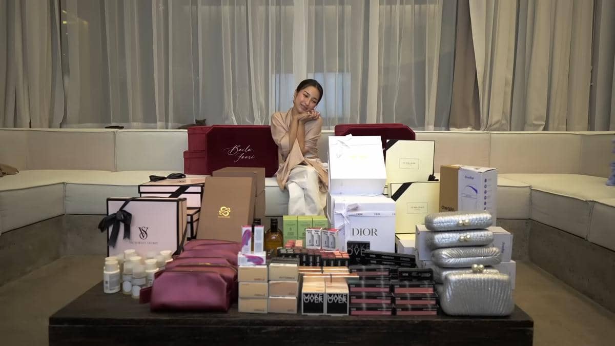 Seorang perempuan duduk di sofa dengan berbagai kotak suvenir bridesmaid berisi produk kecantikan dan hadiah mewah di depannya.