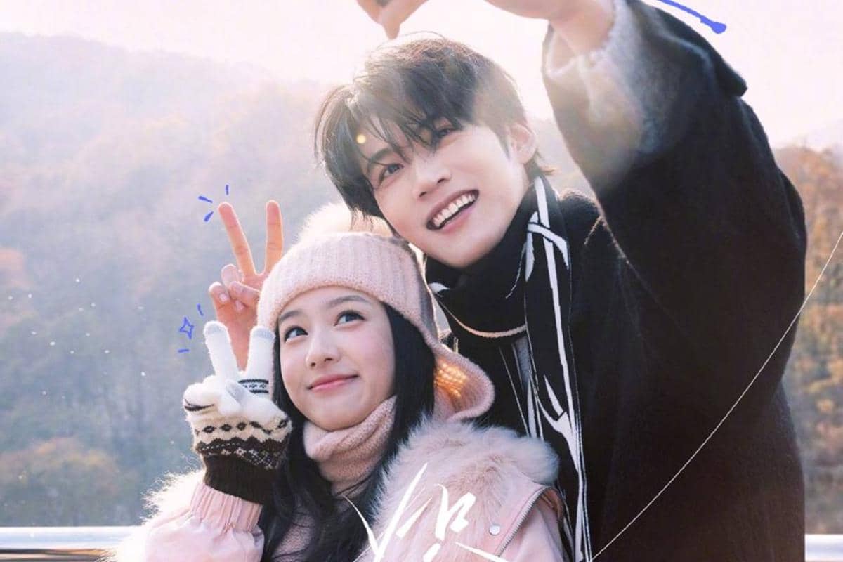 Dua orang mengenakan pakaian musim dingin tersenyum cerah sambil berfoto selfie di luar ruangan dengan latar pegunungan.