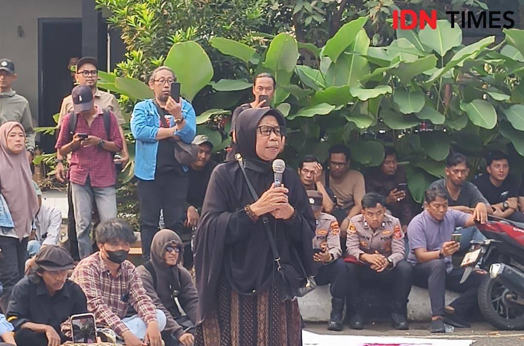 Seorang warga Desa Sukaraja mengenakan kerudung hitam berbicara menggunakan mikrofon di depan pejabat dan warga Kabupaten Bogor.