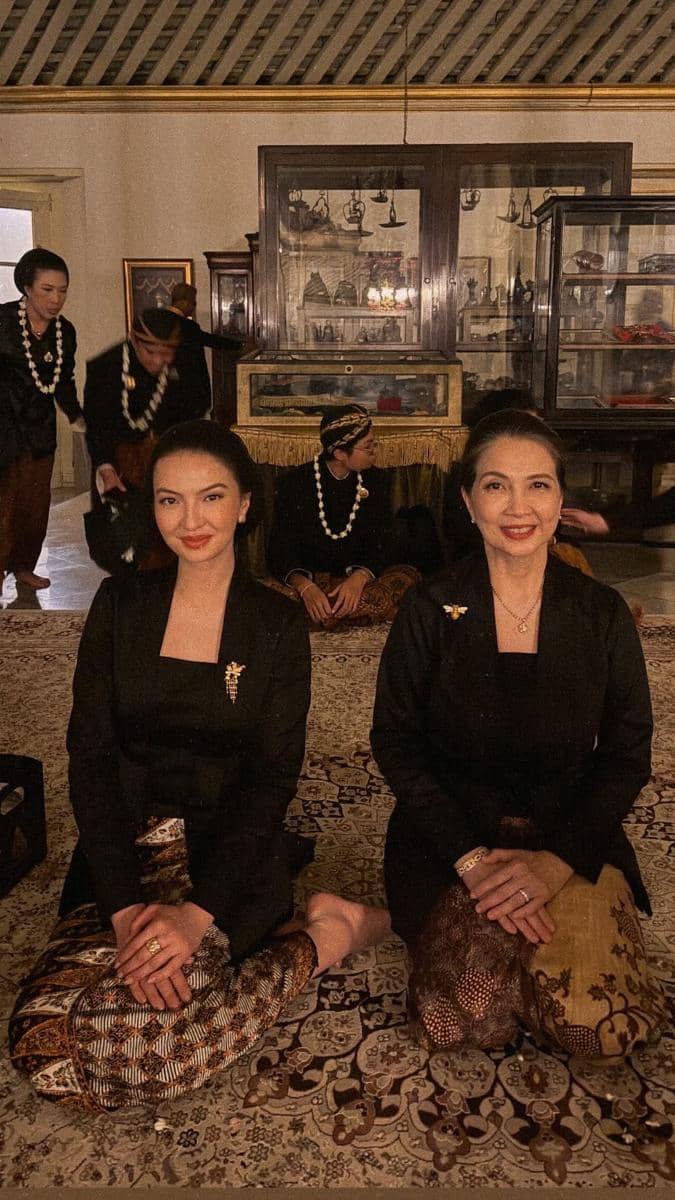 Dua perempuan mengenakan kebaya hitam dan kain batik duduk bersila di dalam ruangan tradisional saat Kirab Pusaka Dalem Malam 1 Suro di Mangkunegaran.