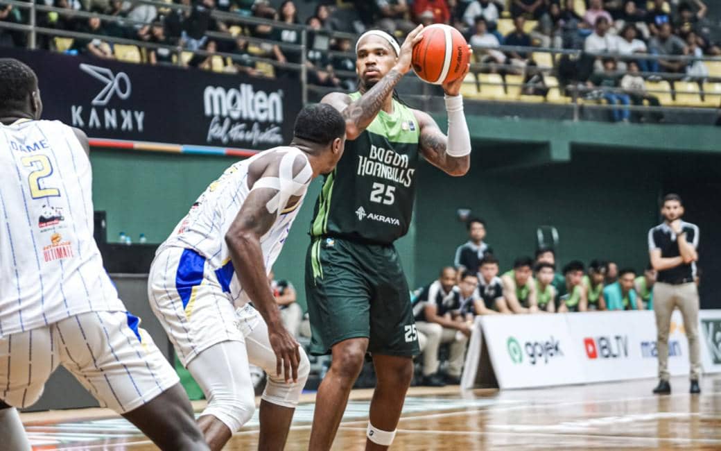 Pemain Bogor Hornbills mengenakan seragam hijau memegang bola basket sambil dijaga pemain lawan dalam pertandingan IBL 2026 di lapangan.