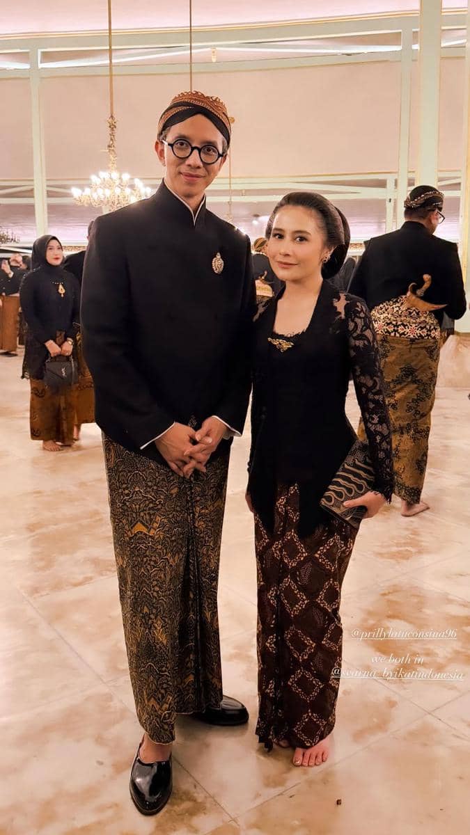 Dua orang mengenakan busana adat Jawa lengkap dengan kain batik dan beskap saat menghadiri Kirab Pusaka Dalem Malam 1 Suro di Mangkunegaran.