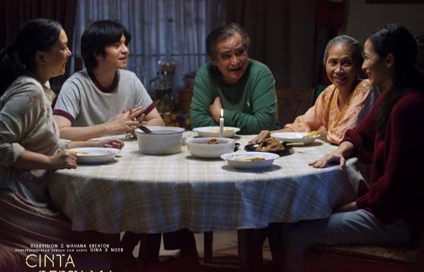 Lima orang duduk di meja makan bundar sambil berbincang hangat dalam suasana keluarga dari film Cinta Pertama, Kedua & Ketiga.