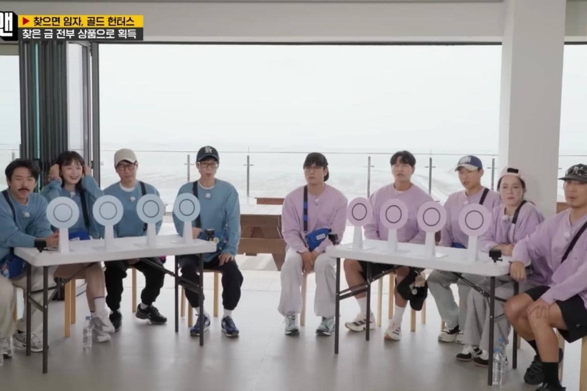Para peserta Running Man episode 774 duduk di dua meja berhadapan mengenakan kaus biru dan ungu muda di ruangan dengan pemandangan laut.