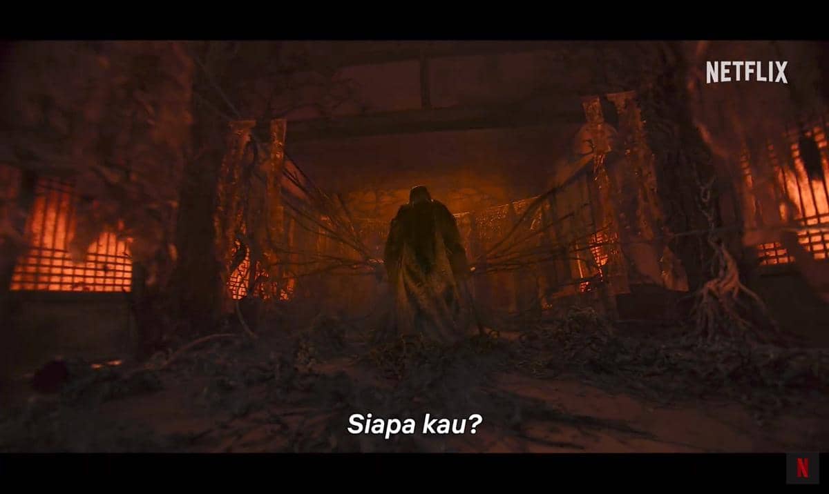 Seorang tokoh berjubah berdiri di ruangan gelap bernuansa merah dengan akar dan ranting menjalar di sekitarnya dalam teaser The East Palace.