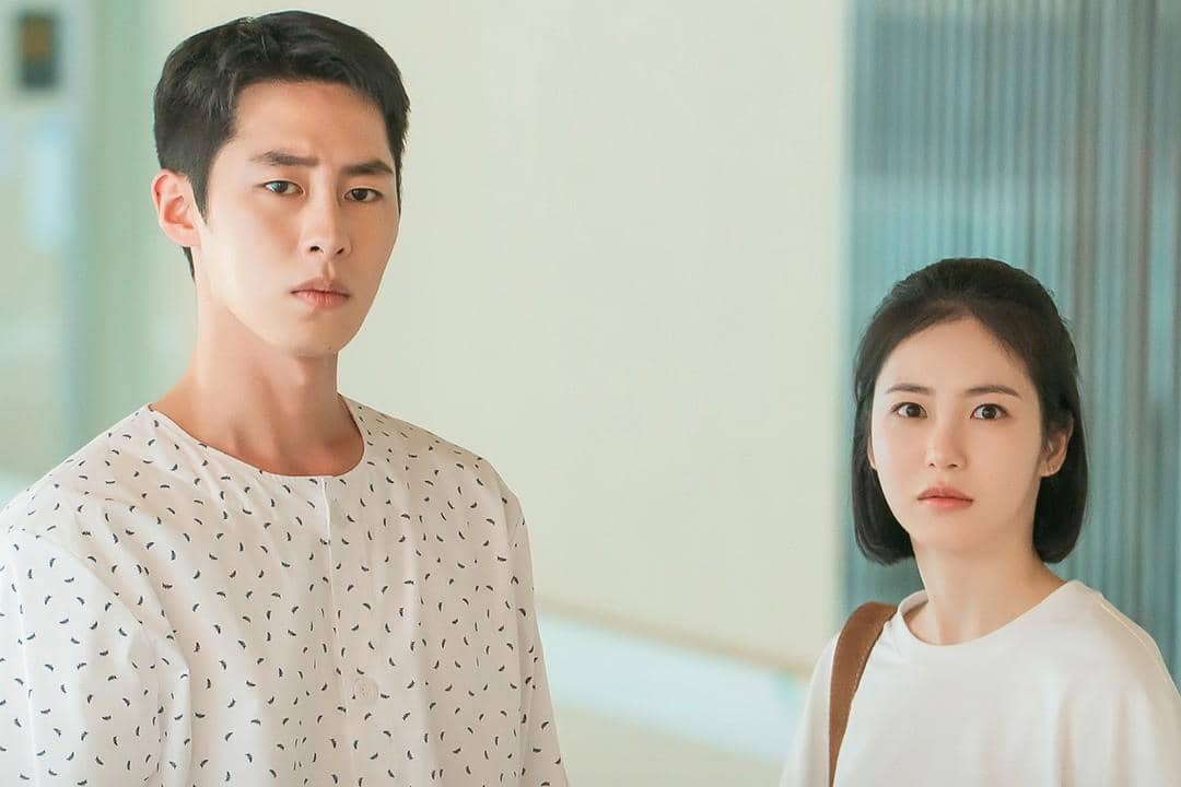 Dua karakter dalam drama Korea Doctor on the Edge berdiri di koridor rumah sakit dengan ekspresi serius dan terkejut.