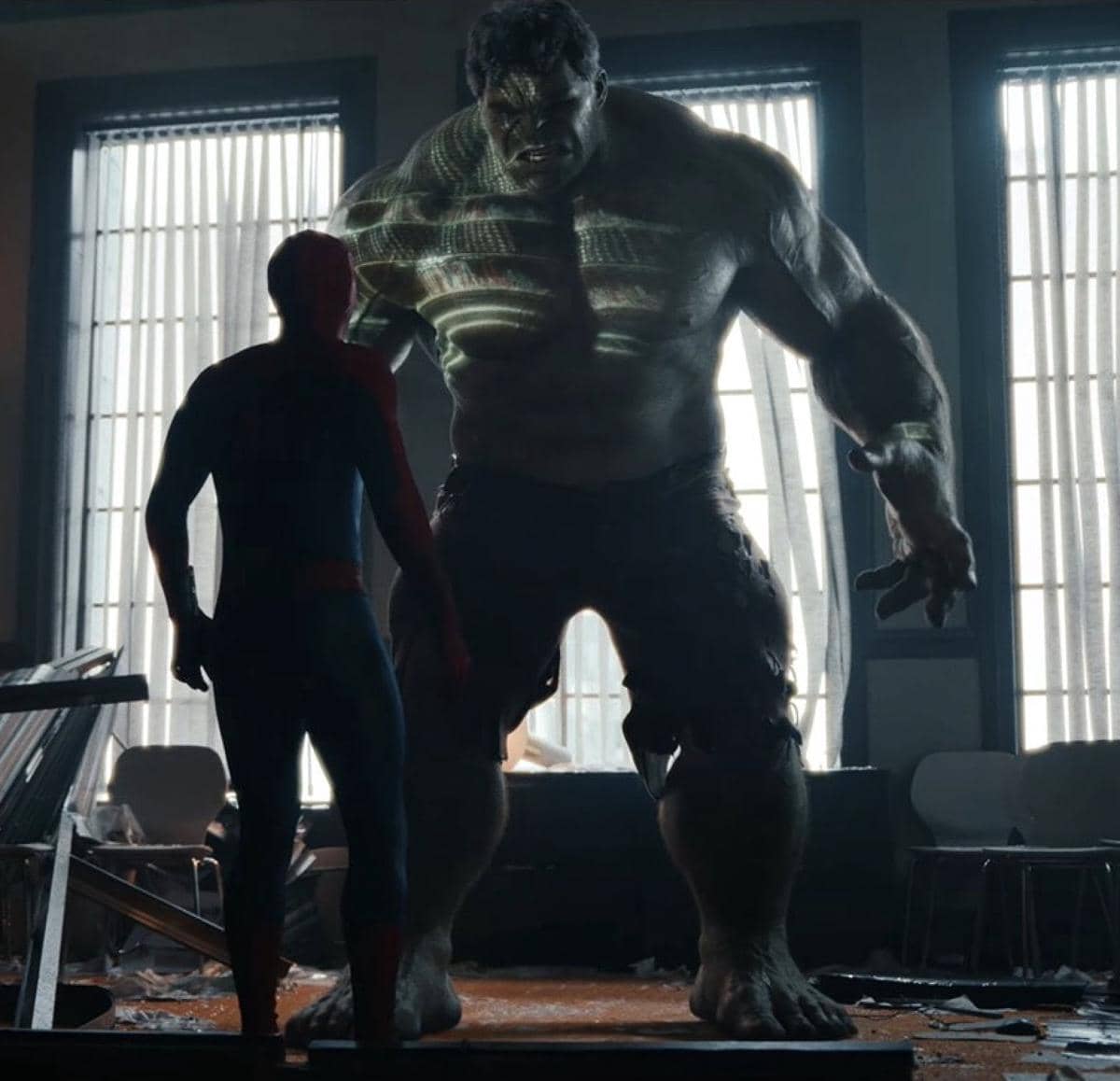Spider-Man berdiri di depan Hulk yang berukuran besar di dalam ruangan dengan cahaya masuk melalui jendela rusak.