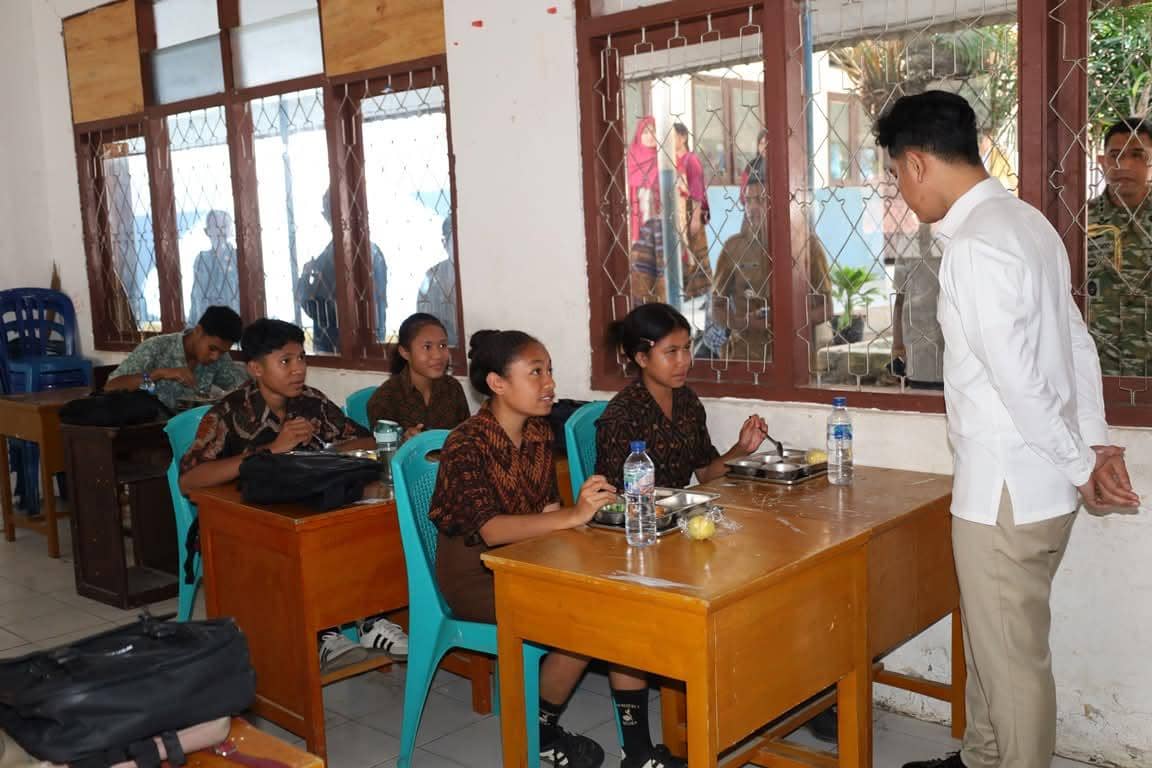 Seorang pejabat berbaju putih berbincang dengan beberapa siswa berseragam batik di dalam ruang kelas SDN Wolomoni Ende.
