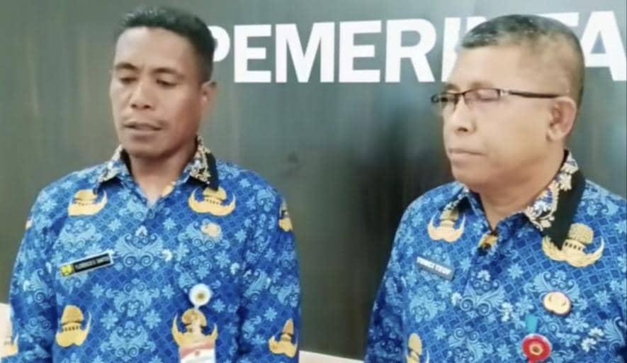 Dua ASN Dinas PUPR Kabupaten Kupang mengenakan seragam batik biru berdiri di depan latar bertuliskan kata 'PEMERINTAH'.