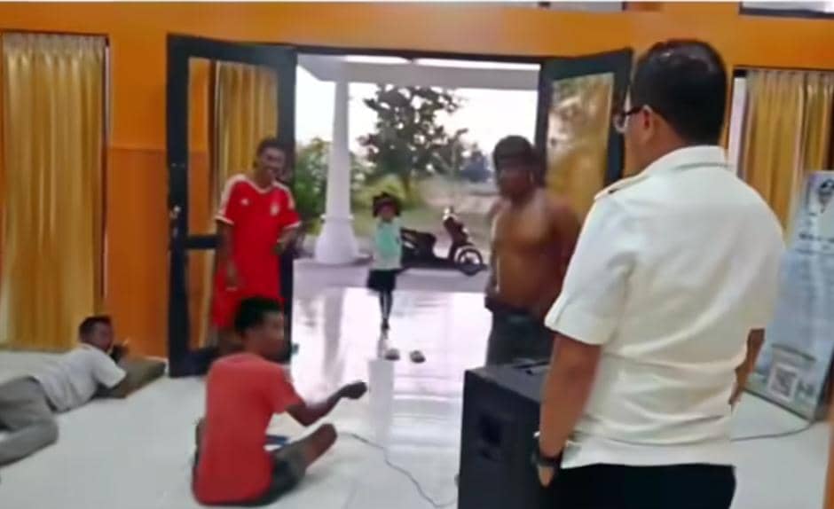Beberapa pria berada di dalam ruangan kantor dengan tirai kuning dan pintu terbuka, salah satu pria berbicara dengan seorang pria berseragam putih.