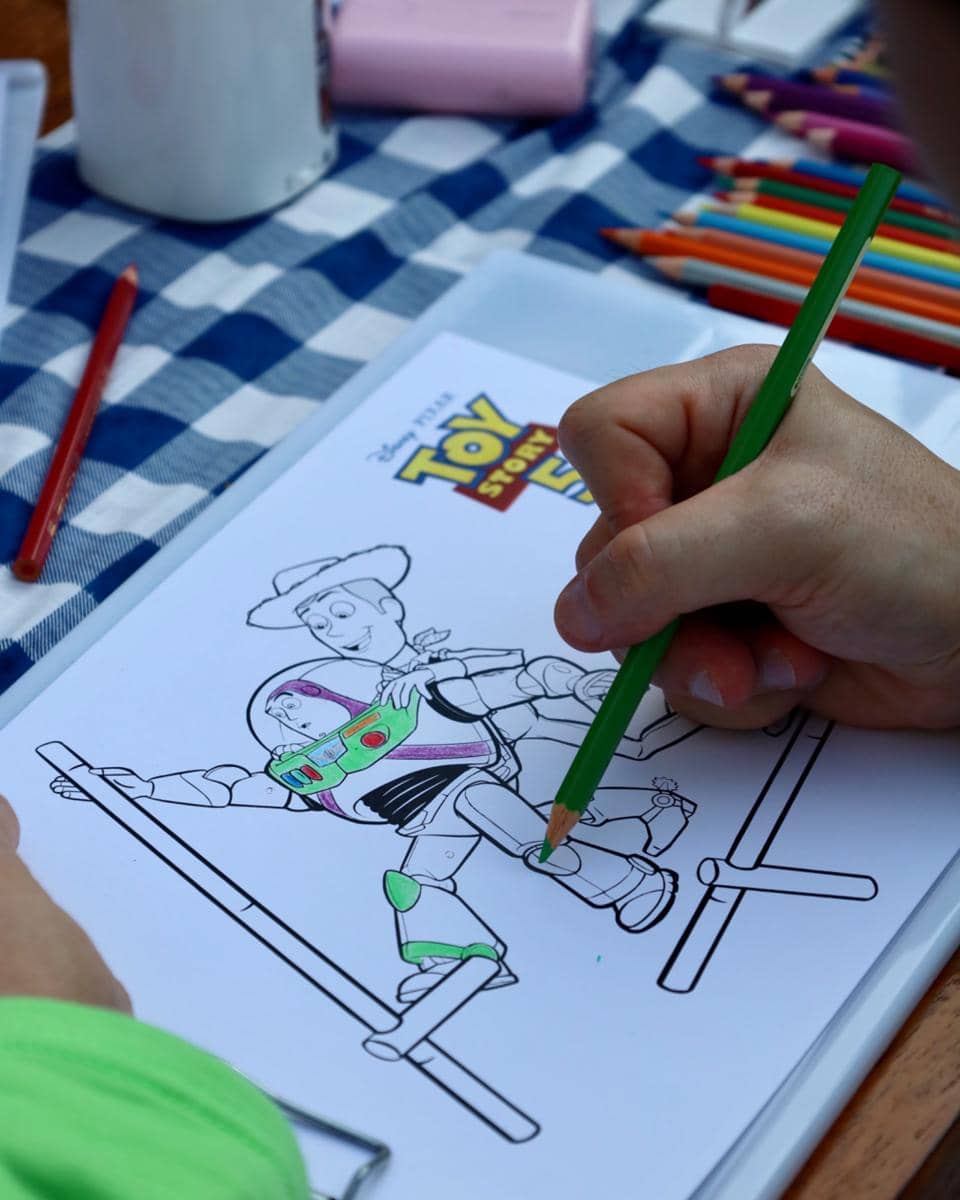 Seorang anak mewarnai gambar karakter Toy Story 5 dengan pensil warna di atas meja beralas kain kotak biru putih di Central Park Mall Jakarta.