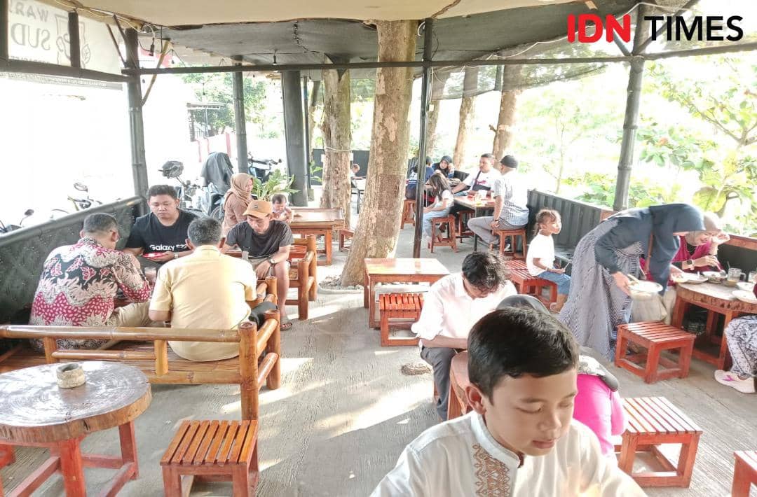 Suasana ramai di Warkop Sudut Bilqila Brebes dengan pengunjung menikmati makanan dan minuman di meja kayu pada sore hari.
