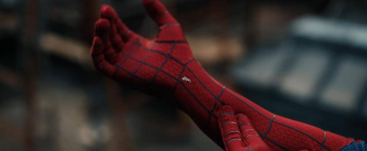 Tangan karakter berkostum Spider-Man berwarna merah dengan pola jaring sedang terlihat dari dekat dalam suasana gelap.
