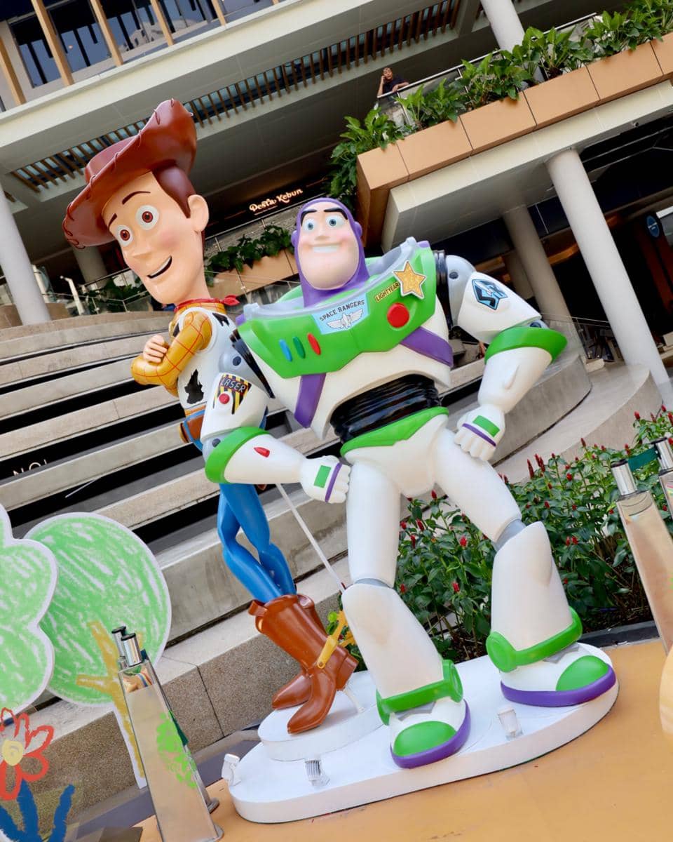 Patung karakter Woody dan Buzz Lightyear dari Toy Story dipajang di area luar Central Park Mall Jakarta dengan latar tangga dan tanaman hias.