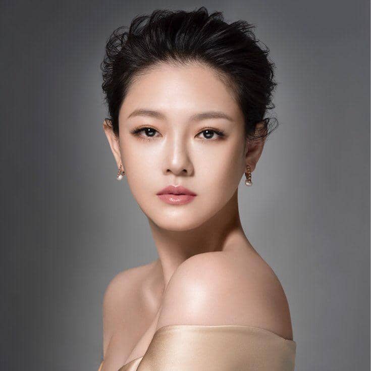 Barbie Hsu berambut pendek bergaya elegan dengan riasan natural dan anting mutiara, mengenakan gaun berwarna krem.