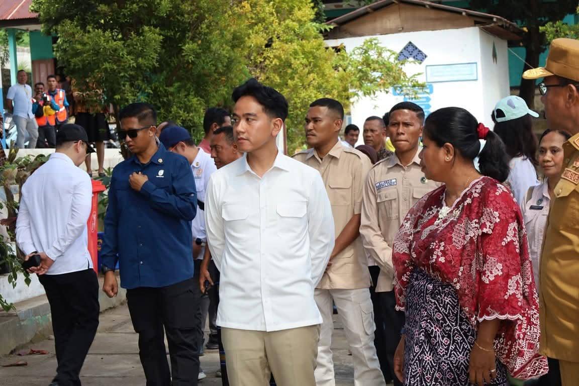 Seorang pejabat mengenakan kemeja putih berdialog dengan warga dan staf sekolah di SDN Wolomoni Ende saat kunjungan program pendidikan.