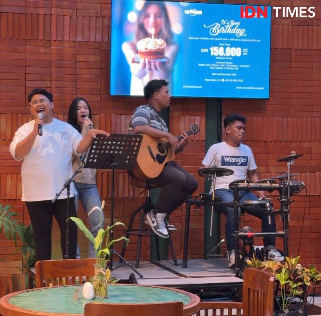Grup musik tampil di Wolon All Day Dining, Lobby Elais by ARTOTEL Medan, dengan penyanyi, gitaris, dan drummer di atas panggung kecil.