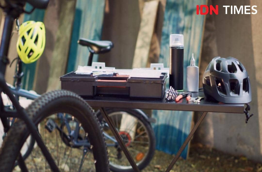 Perlengkapan bersepeda seperti helm, botol minum, dan alat perawatan sepeda diletakkan di atas meja dekat sepeda di area terbuka.