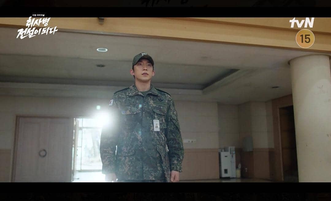 Seorang tentara mengenakan seragam militer berdiri di dalam gedung dengan cahaya matahari masuk dari jendela di drama The Legend of Kitchen Soldier.
