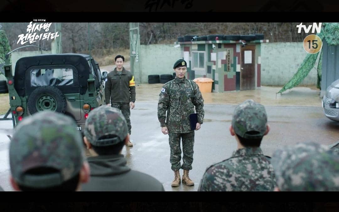 Beberapa tentara berpakaian militer berdiri di area markas dengan kendaraan dan pos jaga dalam cuplikan drama The Legend of Kitchen Soldier.