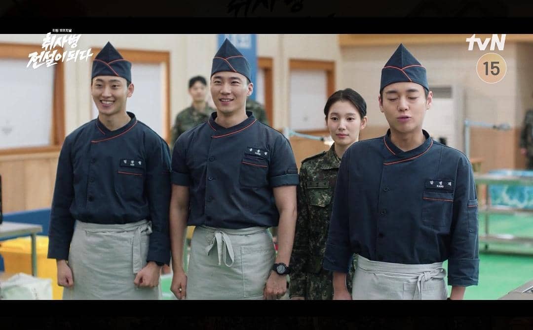 Empat pemeran drama The Legend of Kitchen Soldier mengenakan seragam dapur dan militer berdiri di ruang makan barak tentara.
