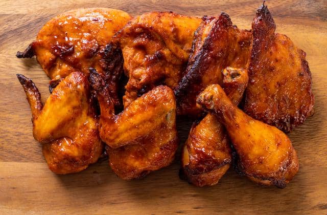 Potongan ayam bakar berwarna kecokelatan dengan bumbu meresap tersaji di atas talenan kayu, tampak menggugah selera.