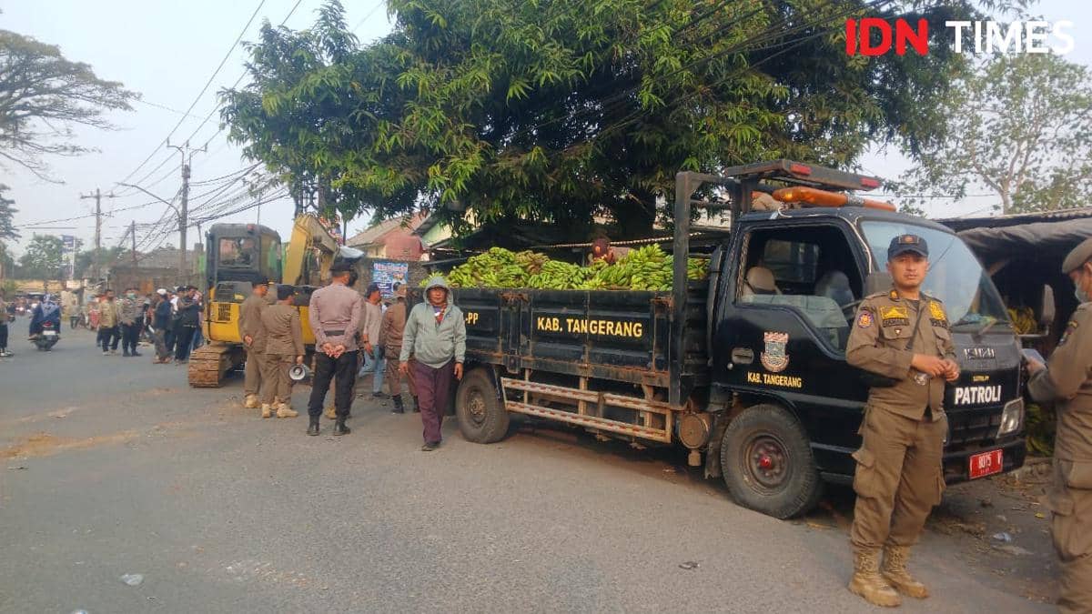 Petugas Satpol PP Kabupaten Tangerang melakukan penertiban pedagang di lahan bekas TPPS dengan truk patroli dan alat berat di lokasi.