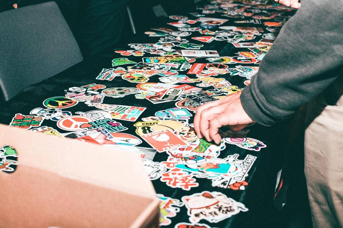 Seseorang memilih berbagai stiker berwarna-warni dengan desain unik yang tersebar di atas meja hitam dalam suasana bisnis kreatif.