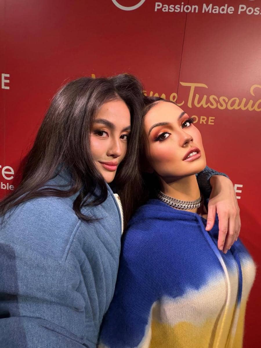 Agnez Mo berpose di samping patung lilin dirinya di Madame Tussauds Singapura dengan latar merah bertuliskan nama museum.