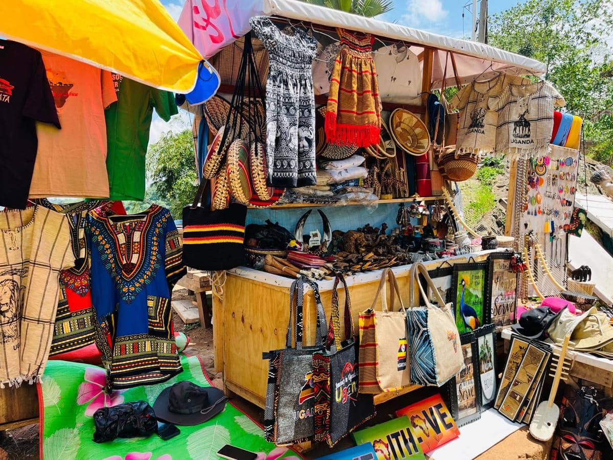 Kios kecil menjual berbagai merchandise warna-warni seperti pakaian tradisional, tas kain, topi, dan suvenir etnik di ruang terbuka.