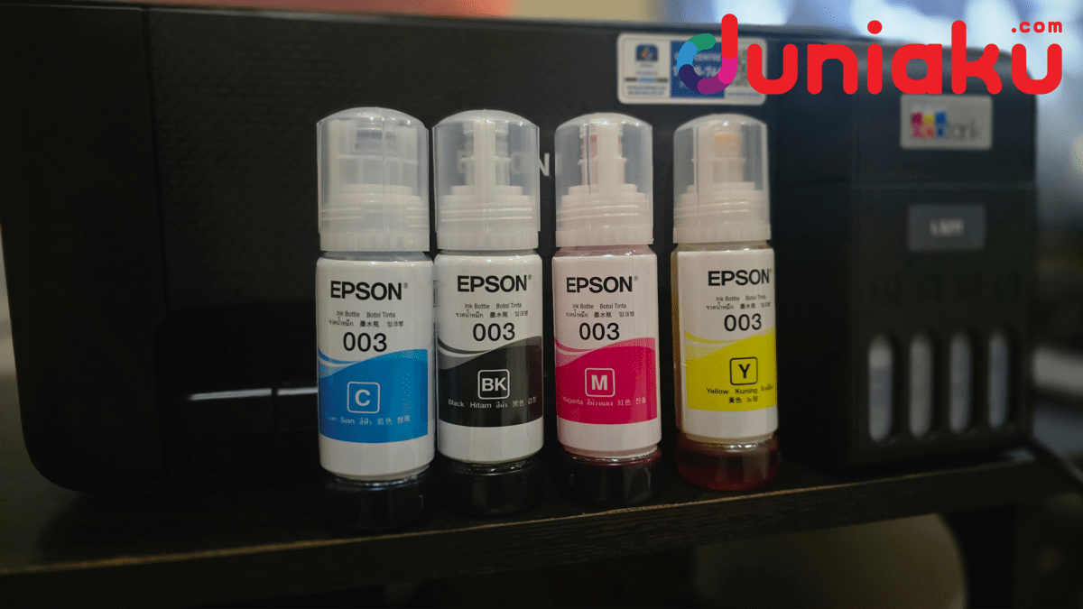 Empat botol tinta Epson 003 warna cyan, hitam, magenta, dan kuning berdiri di depan printer Epson L3211 di atas meja.