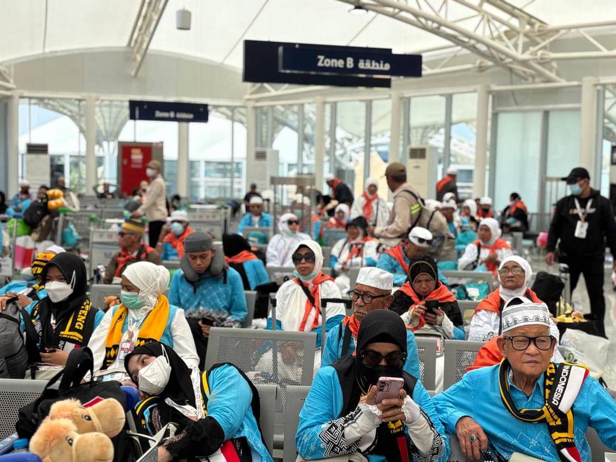 Jemaah haji Indonesia kloter BPN 9 mengenakan pakaian biru dan duduk di ruang tunggu bandara sebelum penerbangan mereka.