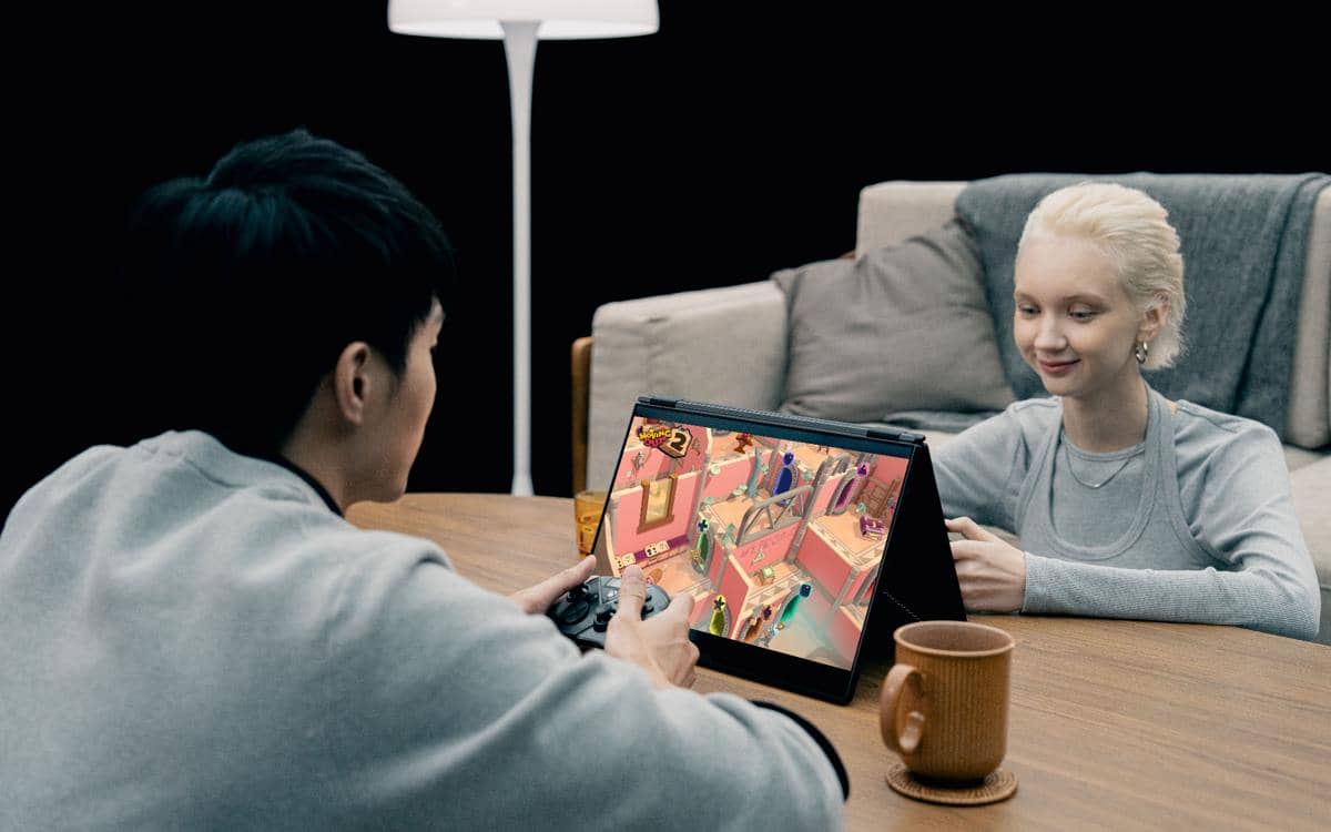 Dua orang bermain game menggunakan laptop ROG Zephyrus Duo dalam mode tenda di atas meja kayu dengan suasana santai di ruang tamu.