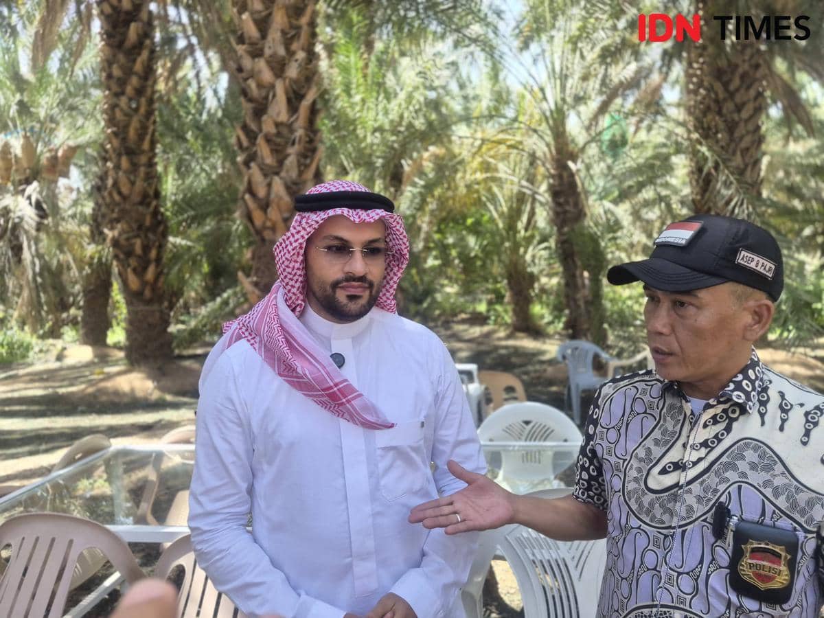 Dua pengelola Kebun Kurma Abdurrahman bin Auf berdiskusi di area kebun yang dipenuhi pohon kurma dan kursi plastik di sekitarnya.