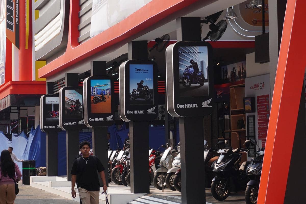 Deretan sepeda motor Honda dipamerkan di sebuah stan dengan papan iklan menampilkan berbagai model motor di area pameran.