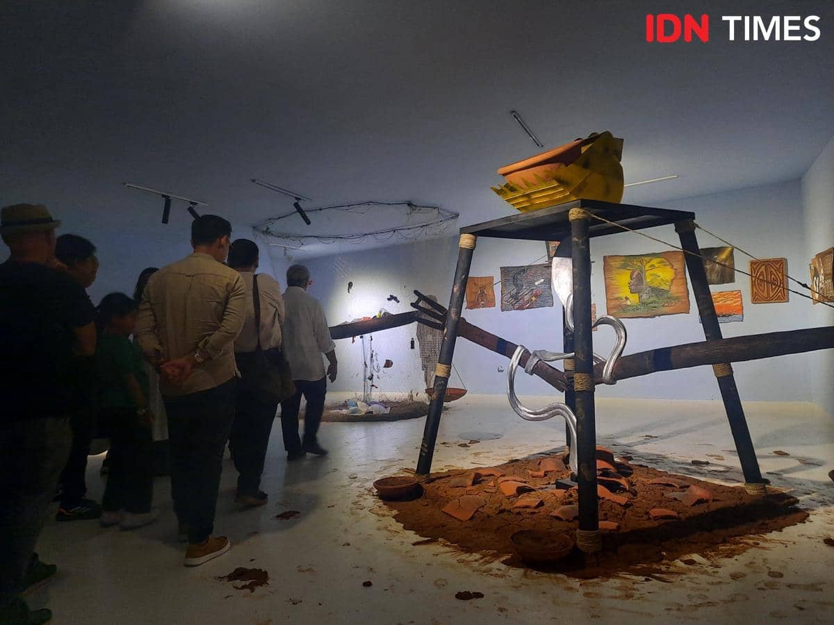Pengunjung melihat instalasi seni kontemporer di ARTJOG 2026 dengan struktur kayu, tanah, dan karya visual di dinding galeri.