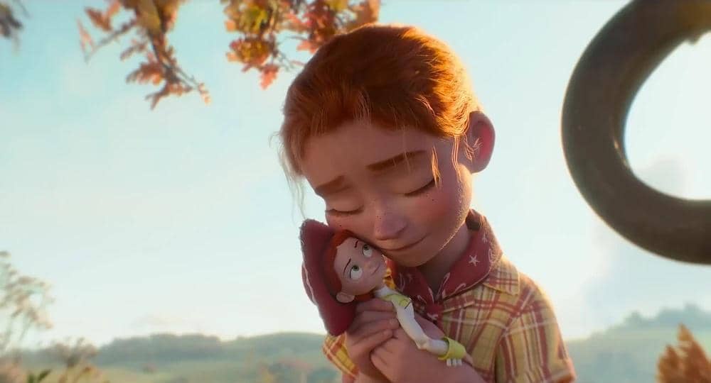 Seorang anak perempuan berambut merah memeluk boneka koboi dengan lembut di bawah pohon pada adegan film animasi Toy Story 5.