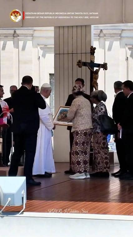 Butet Kertaredjasa menyerahkan bingkai lukisan kepada Paus di Vatikan, disaksikan oleh beberapa orang di area luar ruangan.